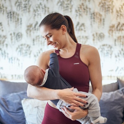 Eine Frau mit roten Klamotten steht in einem Wohnzimmer. Am Arm hält sie ein Baby.
