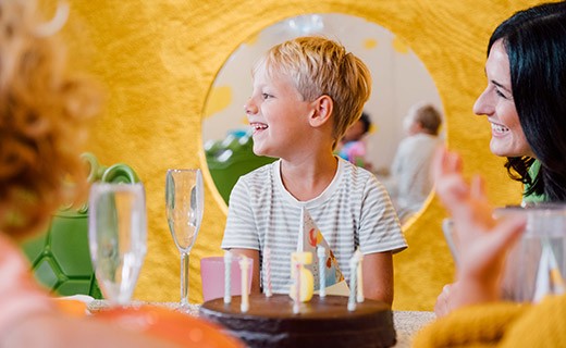 fröhlicher Junge vor der Geburtstagstorte im LOLLIPOP, daneben eine lachende Frau