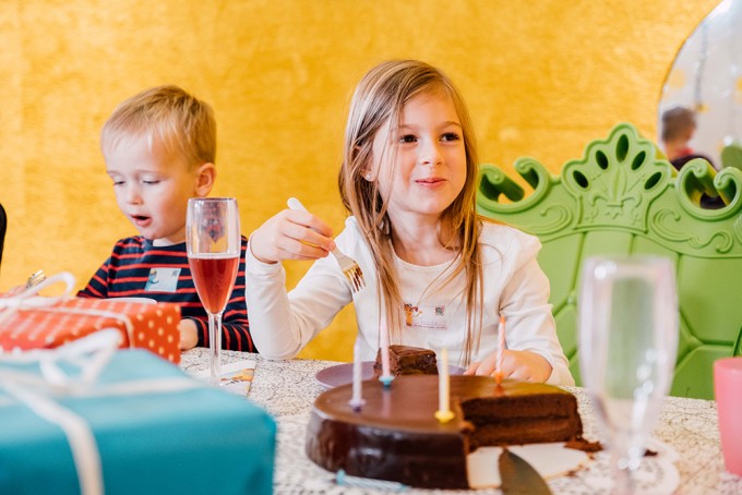 zwei Kinder am Geburtstagstisch mit Geschenken, Sektgläsern und Geburtstagstorte essen Kuchen