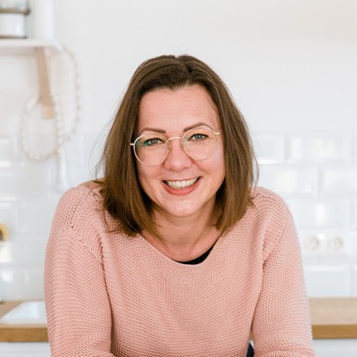 Frau mit schulterlangen, braunen Haaren, einer Brille und einen rosa Pullover.