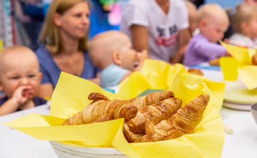 Croissantes in einem Körbchen mit Kleinkindern und Mütter am Frühstückstisch