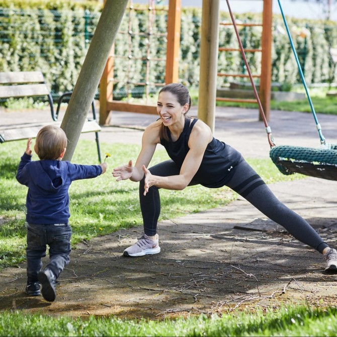 Frau, die auf einem Spielplatz eine Yoga Übung macht. Zu ihr kommt ein kleiner Junge, der ihr eine Blume schenkt.