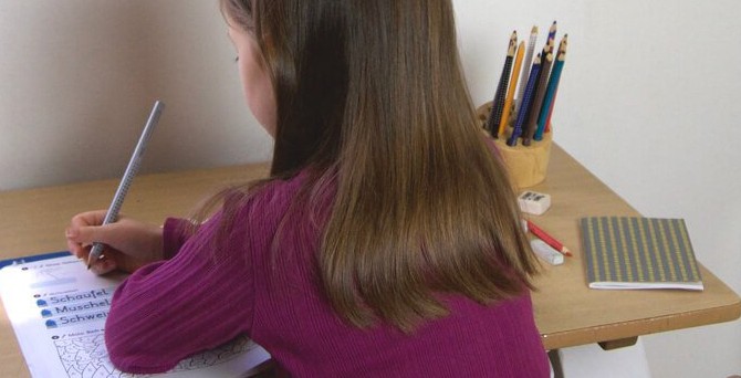 Kleines Mädchen macht in einem Heft eine Aufgabe.