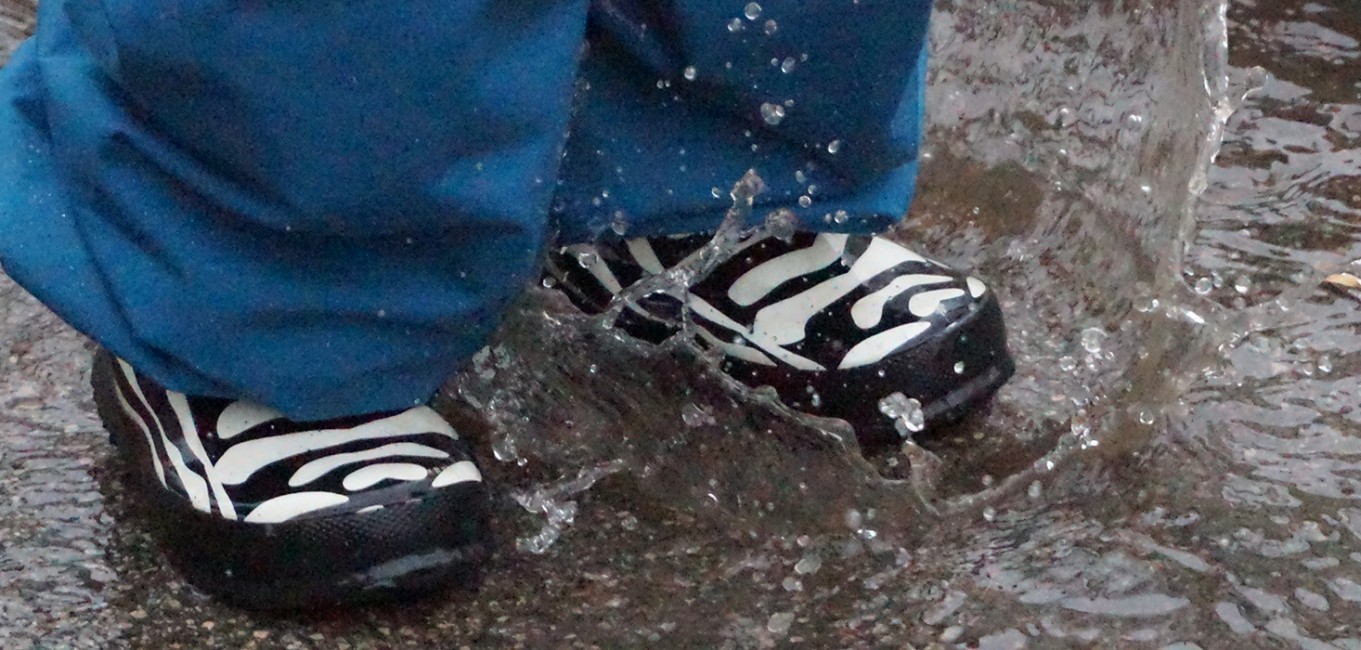 Kind steht mit Gummistiefel in einer Wasserpfütze.